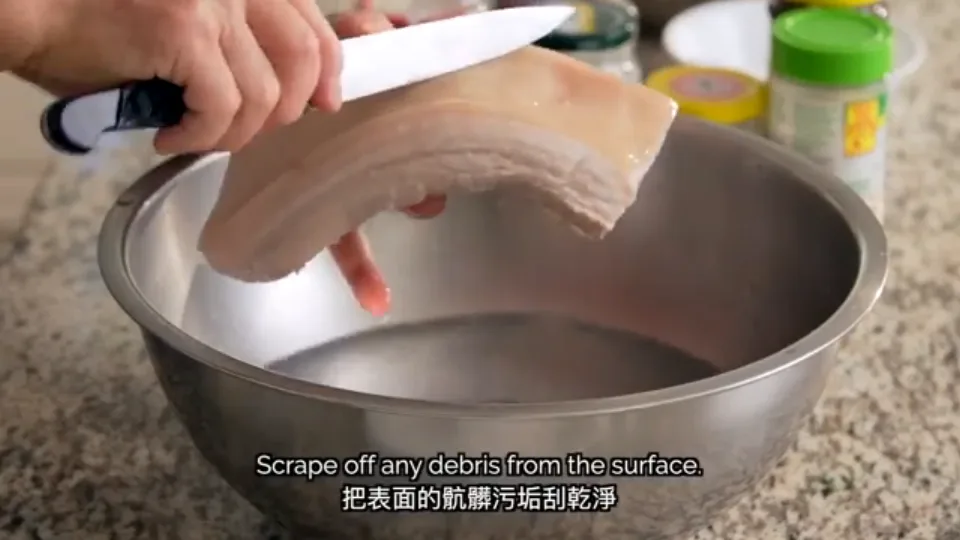Scraping dirt and fine hairs off the pork belly skin with a cleaver in cold water