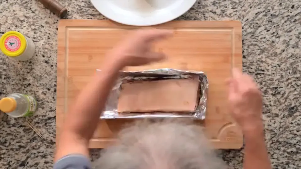 Folding aluminum foil snugly around the sides of the pork belly with the skin facing up