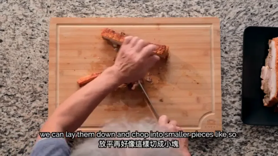 Chopping a strip of crispy roast pork belly on its side into bite-sized pieces with a cleaver