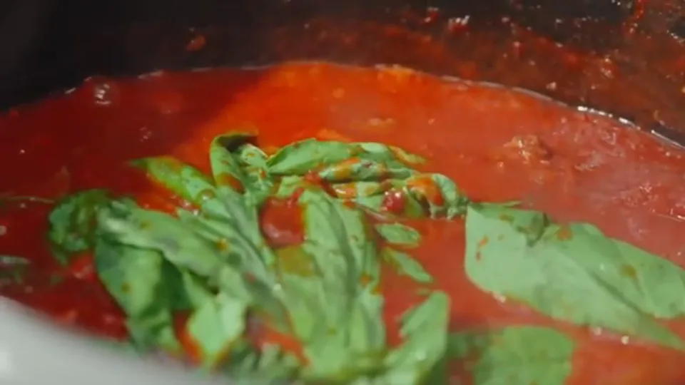 Simmering rich red sauce with fresh basil leaves