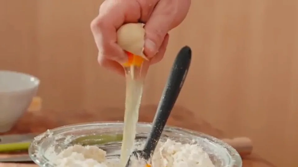 Cracking eggs into seasoned ricotta cheese bowl