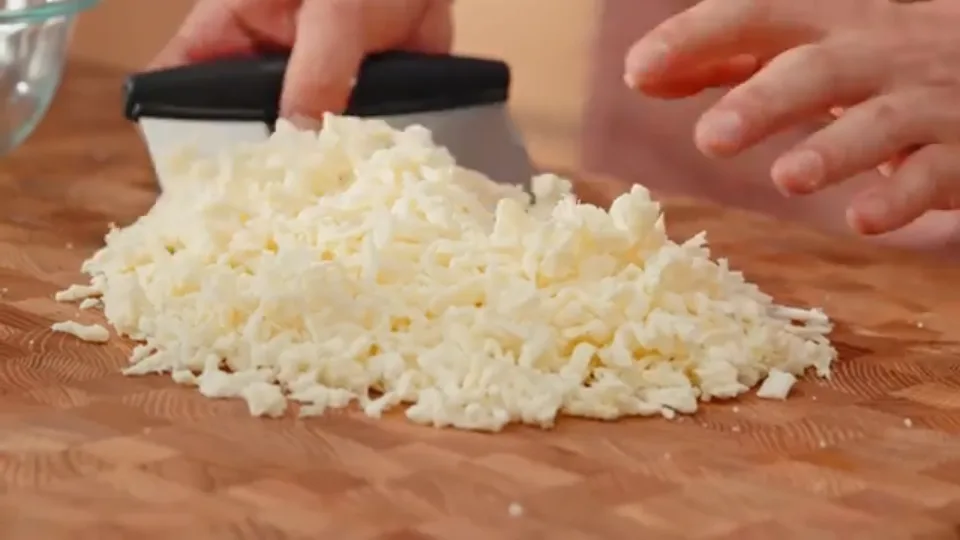 Shredded mozzarella strands grated lengthwise on cutting board